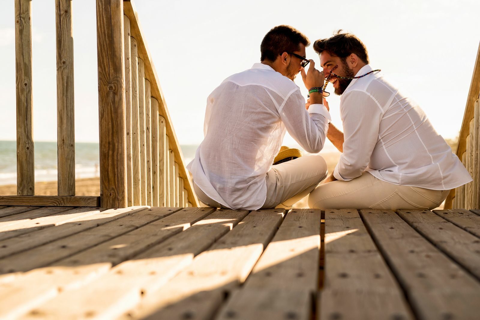 A joyful couple enjoys a sunny day on a wooden deck by the beach, capturing happiness and togetherness.